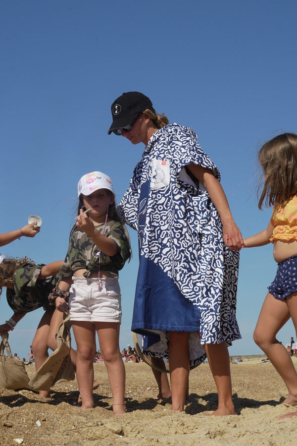Maud Le Car wearing a Save La Mermaid poncho with children on the dunes